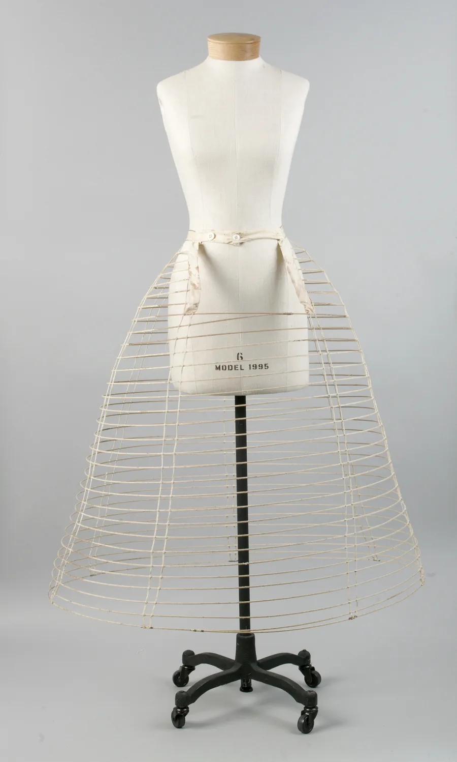 Eine Krinoline von etwa 1860 auf einem Ständer: Ringe aus mit Baumwolle bezogenem Metall, die zum Saum hin weiter werden, gehalten von senkrechten Bändern (The Metropolitan Museum of Art, gemeinfrei)