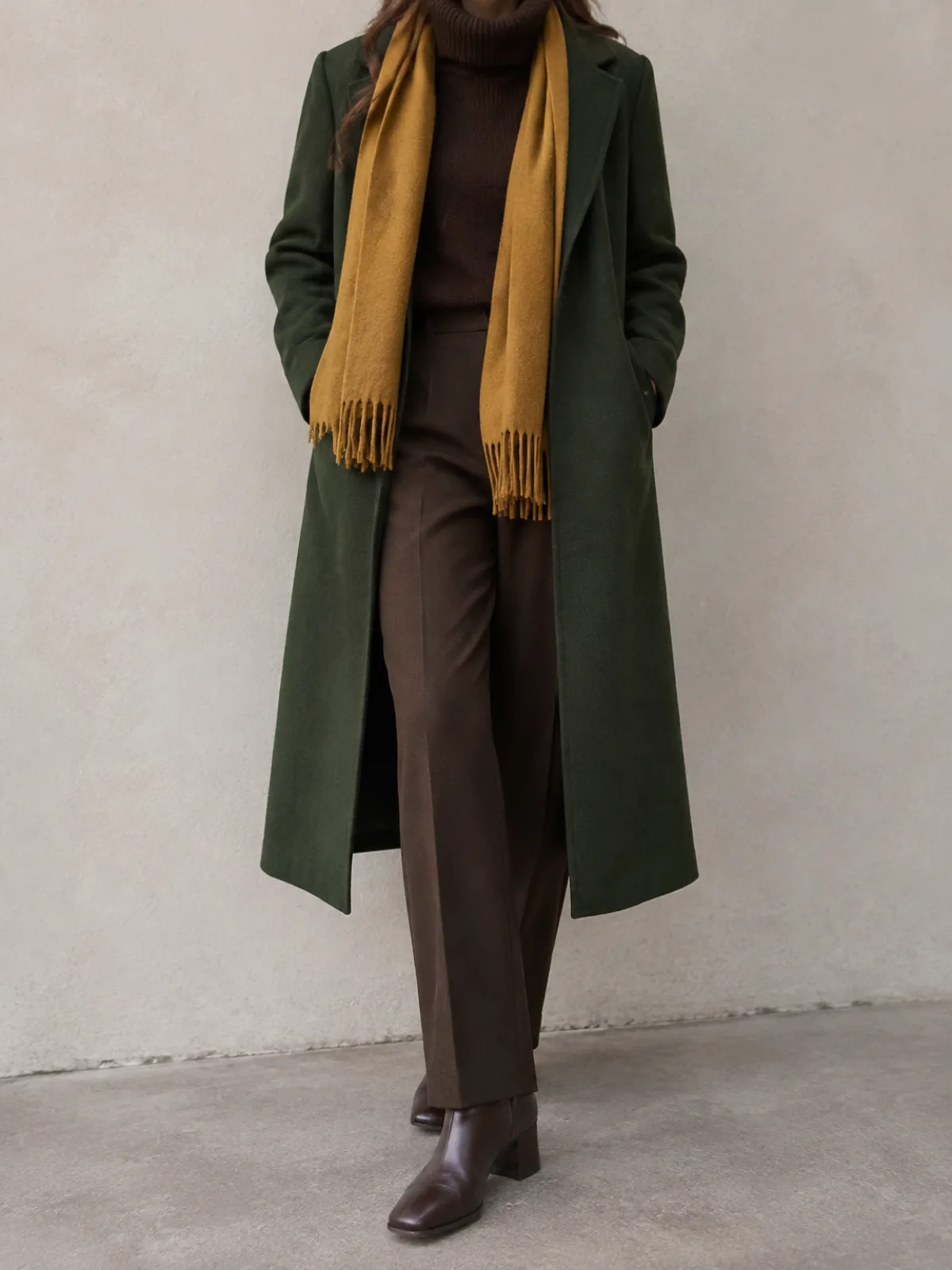 Deep Autumn cold weather outfit: long forest green wool coat, mustard gold scarf, espresso trousers and dark brown boots