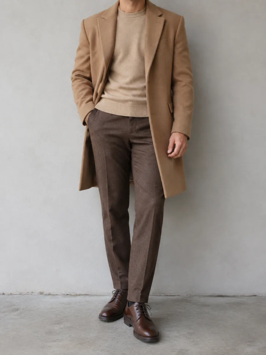 Mann in einem Mantel in Camel über einem Pullover in warmem Beige